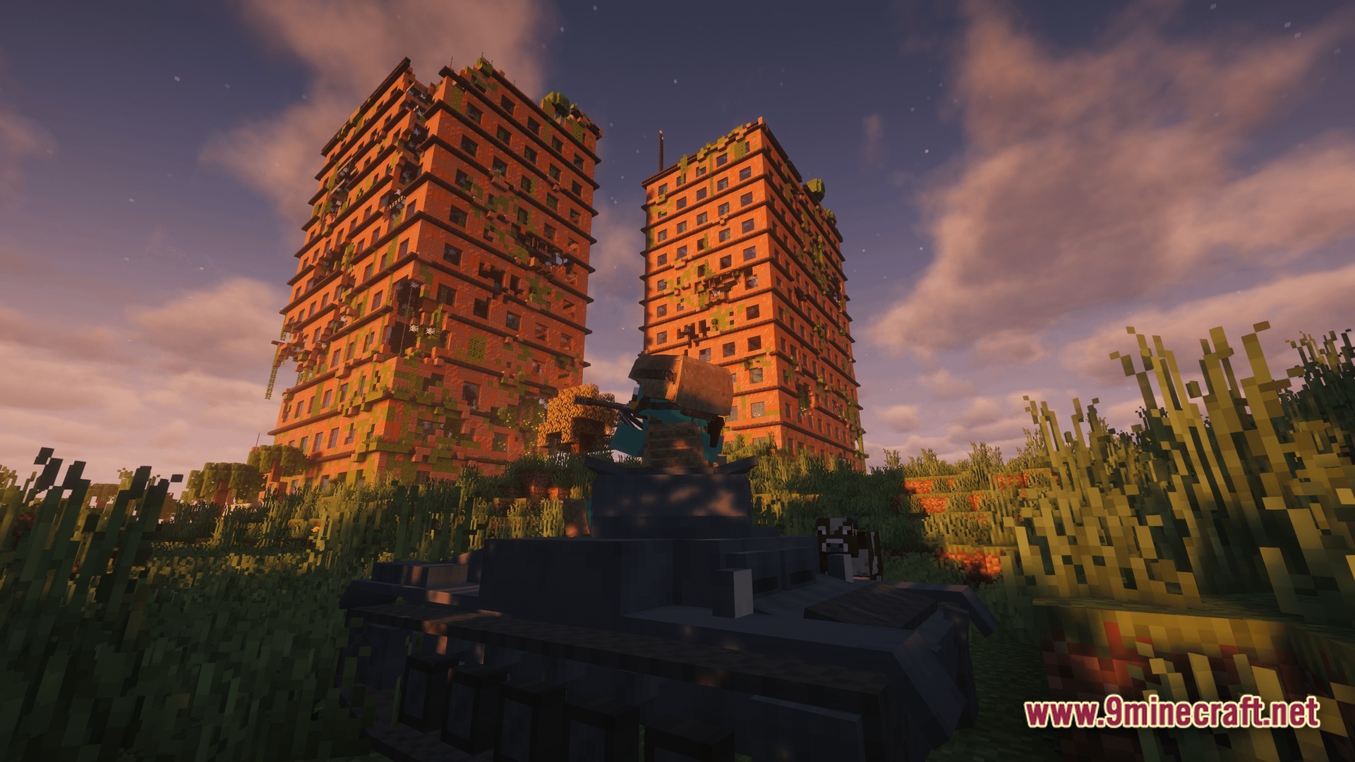 A player operates a tank in a grassy field before two abandoned, vine-covered apartment buildings