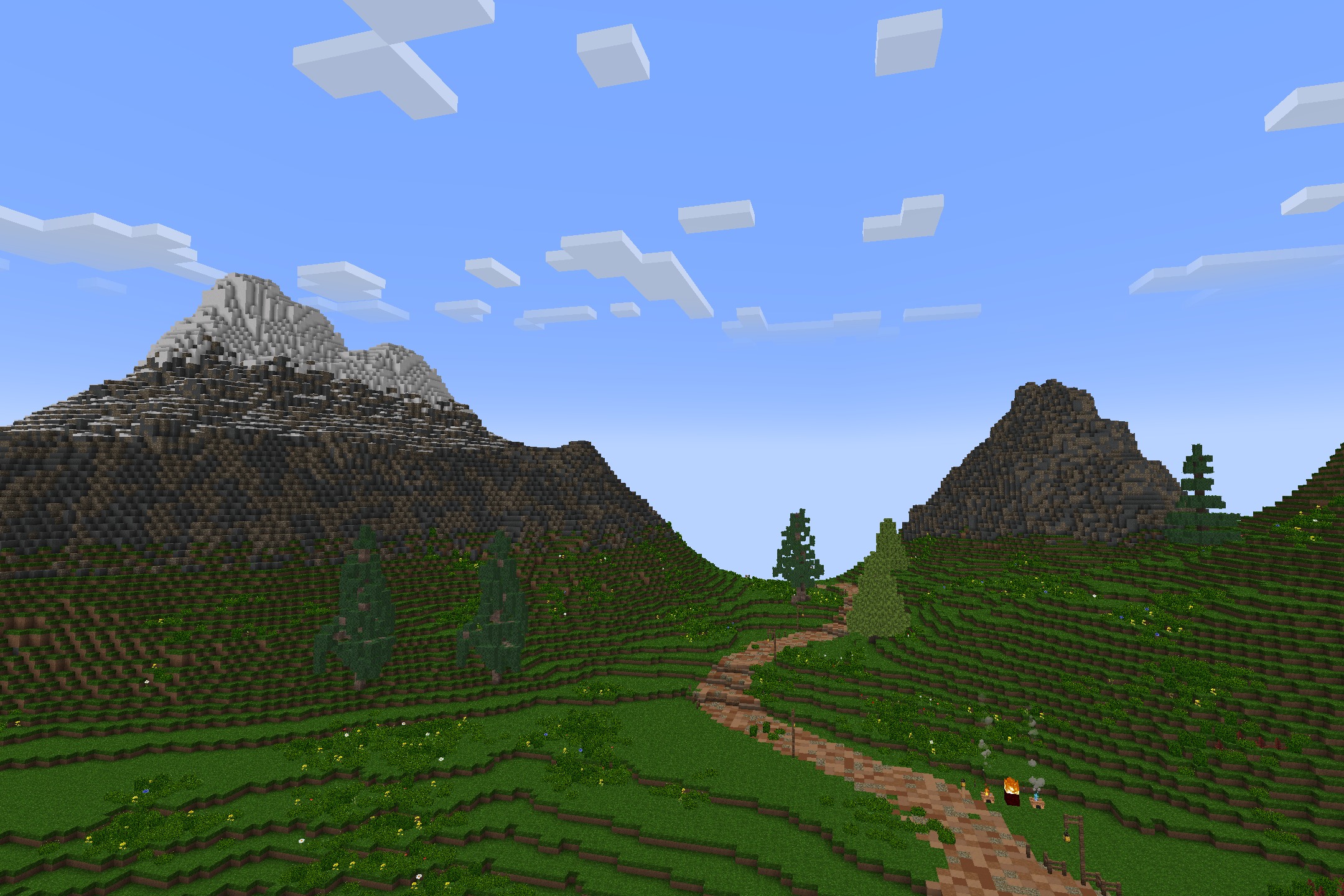 A winding dirt path leads through green hills toward snowy mountains in Minecraft