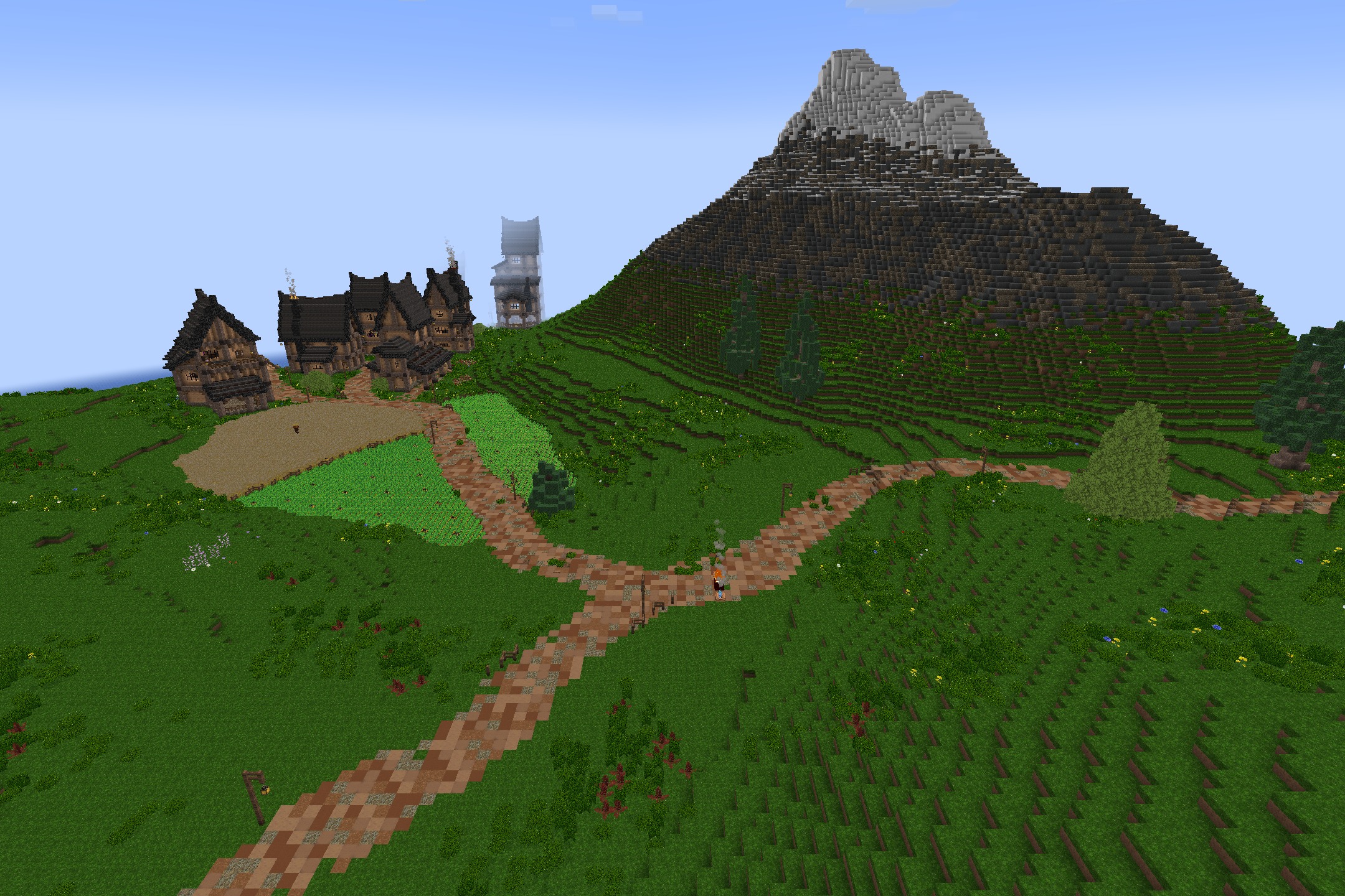 A dirt path splits toward a small village near a large mountain
