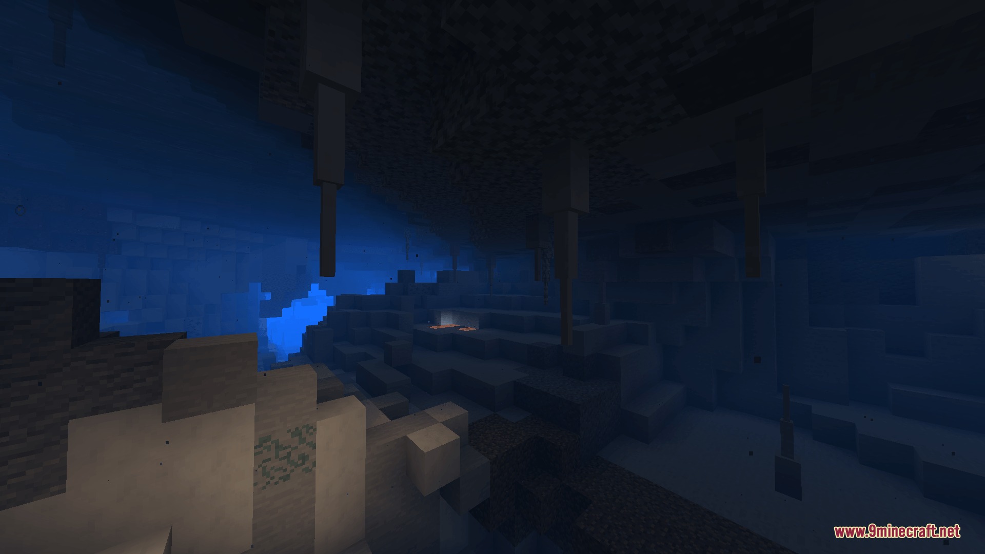A vast underground cavern with stalactites hanging from the ceiling in blue light