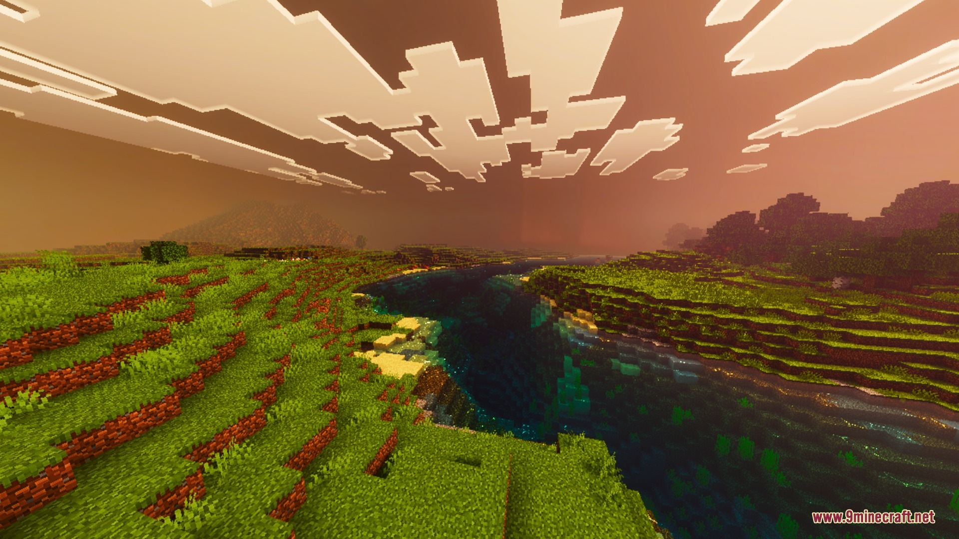 A scenic river valley with green grass under a glowing orange sky