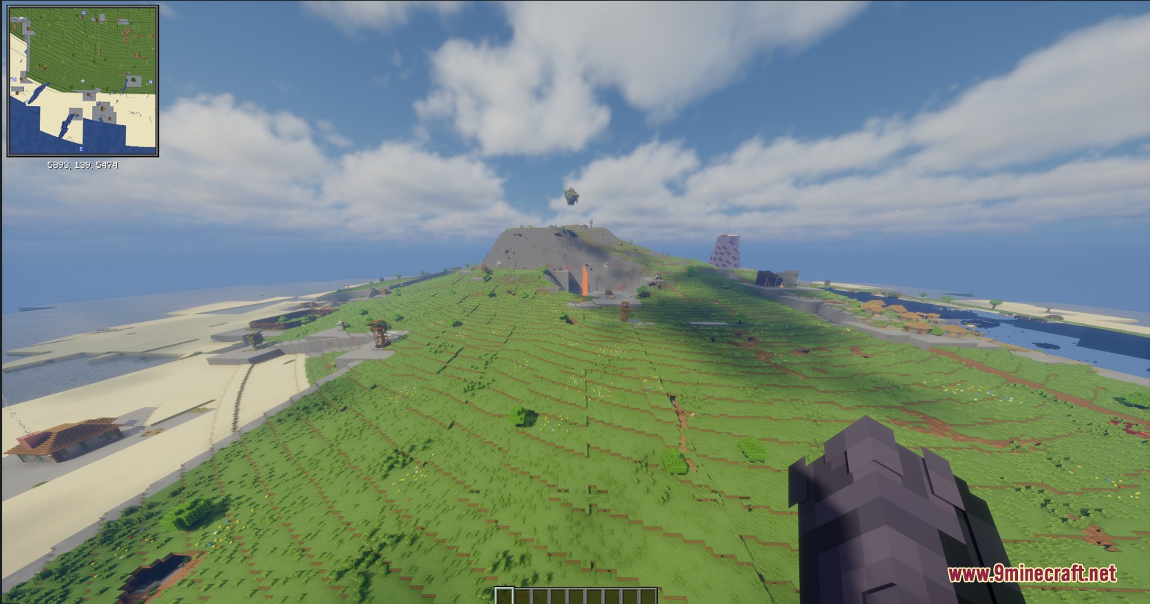 A vast green island landscape with a mountain and small buildings