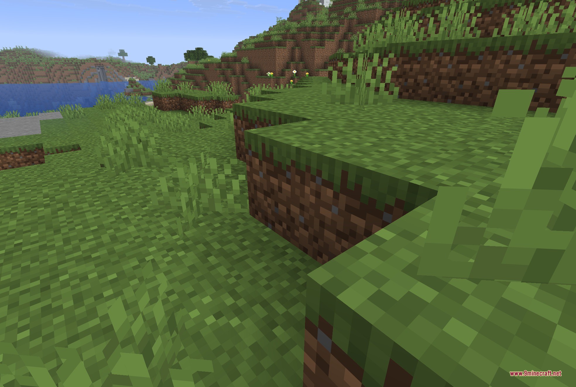 JackFredLib 9minecraft Mod Screenshot 1 A detailed view of grass blocks on a hill with water in distance