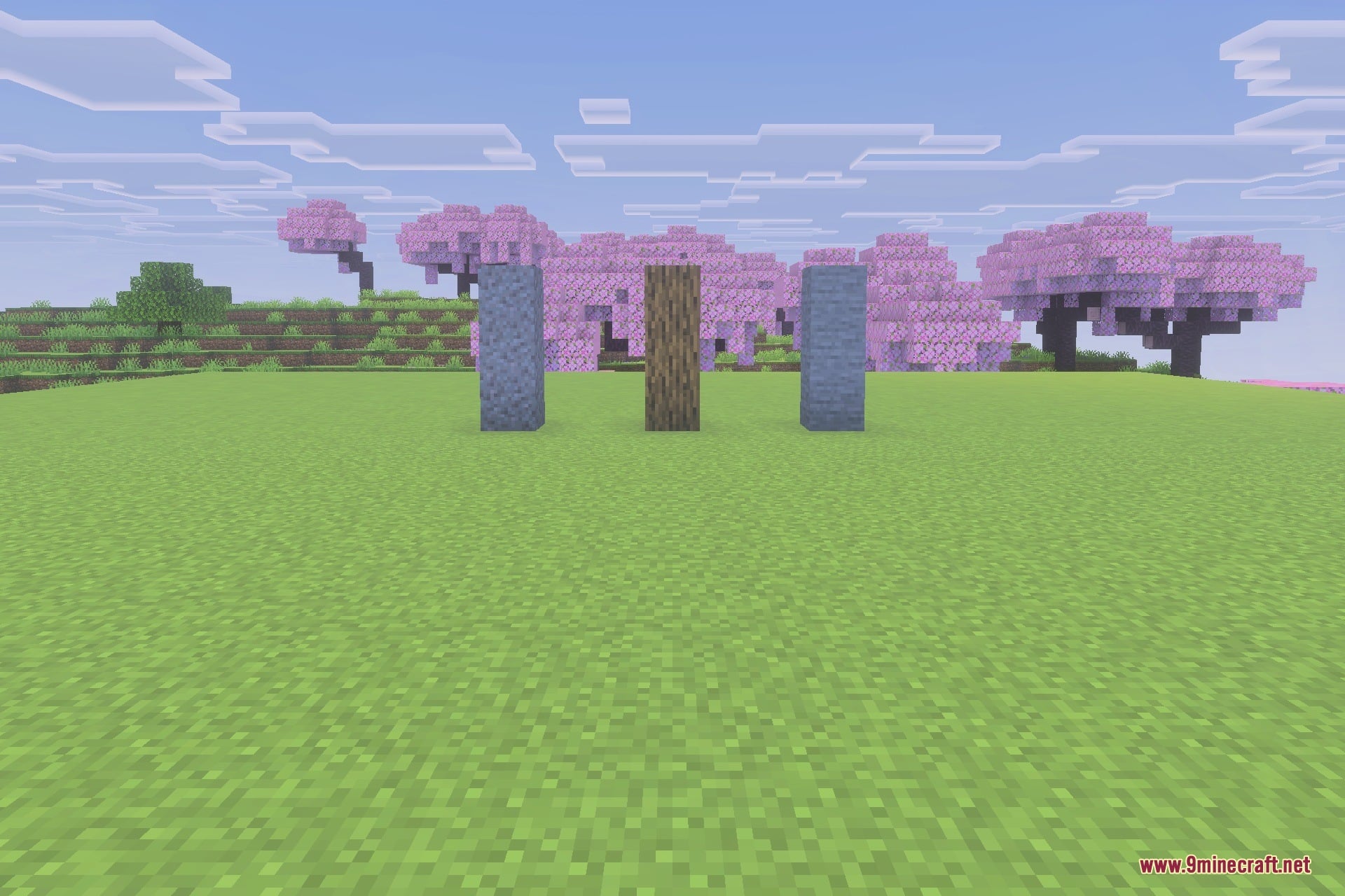 Three vertical pillars stand on a flat grass field with cherry blossom trees