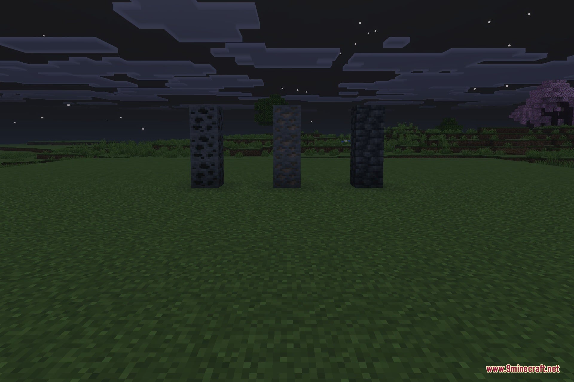 Three dark stone pillars stand in a flat field under cloudy night sky