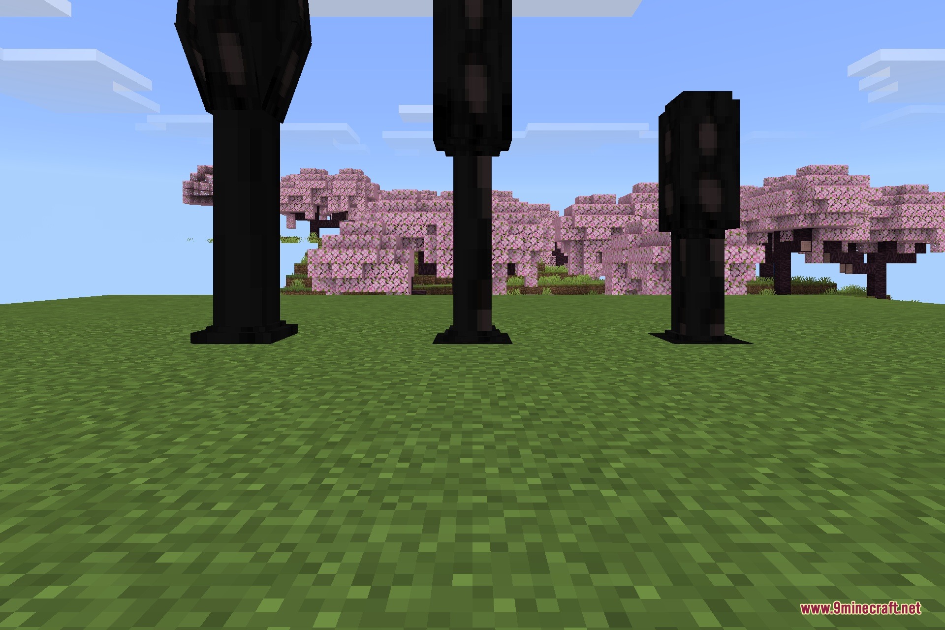 Three tall dark infected pillars standing in a grassy field near cherry trees