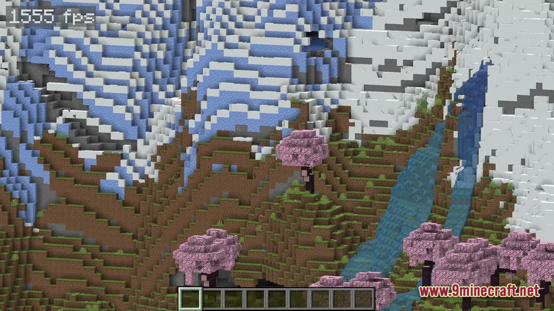 Cherry blossom trees grow on a grassy hillside next to a waterfall and snowy mountain peaks
