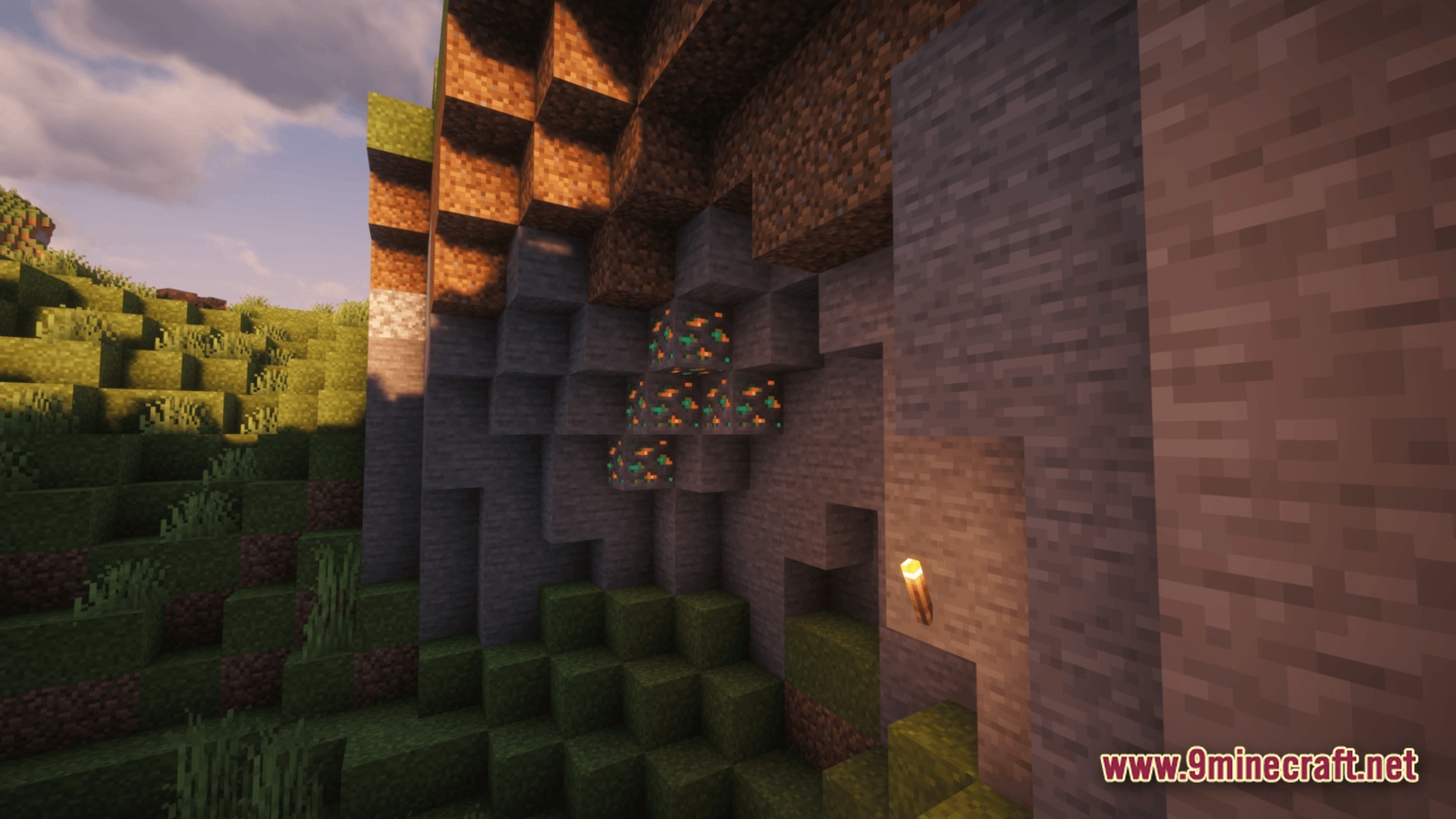 Copper ore blocks embedded in a stone cliffside next to a lit torch at sunset